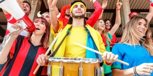 Soccer fan supporters cheering and watching football cup match at intenational stadium bleachers - Sport concept with young people group with multicolor t-shirts having excited fun world championship